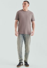 Graues Kurzarm-T-Shirt, getragen mit gefärbten blauen Jeans und schwarzen Turnschuhen mit weißen Akzenten. Einfaches Design, bequeme Passform, lässiger Stil.