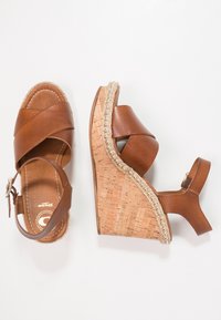 Sandali wedge in pelle marrone con fasce incrociate, tacco in sughero e dettagli intrecciati lungo la suola. Include una cinturino alla caviglia regolabile.