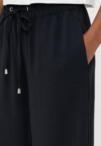 Pantaloni blu navy in tessuto texture, con una cintura elastica dotata di un nodo di corda e dettagli in metallo argentato, tasche laterali.