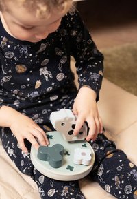 Peuter in ruimte-thema pyjama's speelt met een houten puzzel, waarbij een koe-vormig stuk op een ronde plaat met klavervormen wordt gelegd.