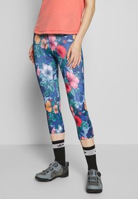 Bloemmotief capri-legging in blauw met roze, oranje en witte bloemen. Gepaard met een koraal T-shirt en grijze wandelschoenen.