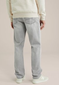 Lichtgrijze denim jeans met een rechte fit, voorzien van twee achterzakken en subtiele wassing. Gepaard met een crèmekleurige sweatshirt en witte sneakers.