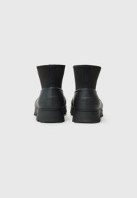Bottes de cheville noires imperméables avec une semelle en caoutchouc texturée et un dessus en tissu extensible. Les caractéristiques incluent un talon solide et aucun matériel visible.