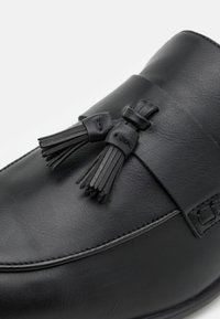 Czarne skórzane buty o gładkiej fakturze, z ozdobnym paskiem i dwoma skórzanymi frędzlami. Okrągły czubek i przeszycia.