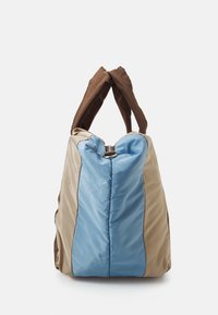 Sac fourre-tout marron et beige avec un panneau central bleu, présentant une texture douce, deux poignées en tissu épaisses et une fermeture supérieure sécurisée.