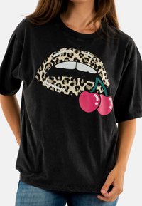Zwarte T-shirt met een grafische afbeelding van een mond in panterprint en twee rode kersen. Korte mouwen, ontspannen pasvorm en een zachte textuur.
