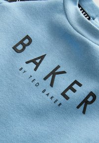 Sudadera azul clara con una textura suave, que presenta las letras negras en negrita "BAKER" y "by TED BAKER" en una fuente moderna.