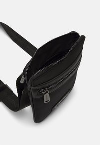 Borsa a tracolla nera in nylon con comparto principale con zip, tasca frontale con zip e tracolla con logo in rilievo.