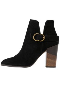Botín de ante negro hasta el tobillo con puntera puntiaguda, corte lateral y un acento de hebilla circular dorada. Presenta un tacón bloque texturizado con aspecto de madera.