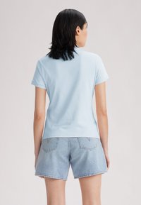 T-shirt bleu clair à manches courtes avec un design ajusté, fabriqué en tissu doux. Associé à un short en denim bleu clair avec des poches arrière.