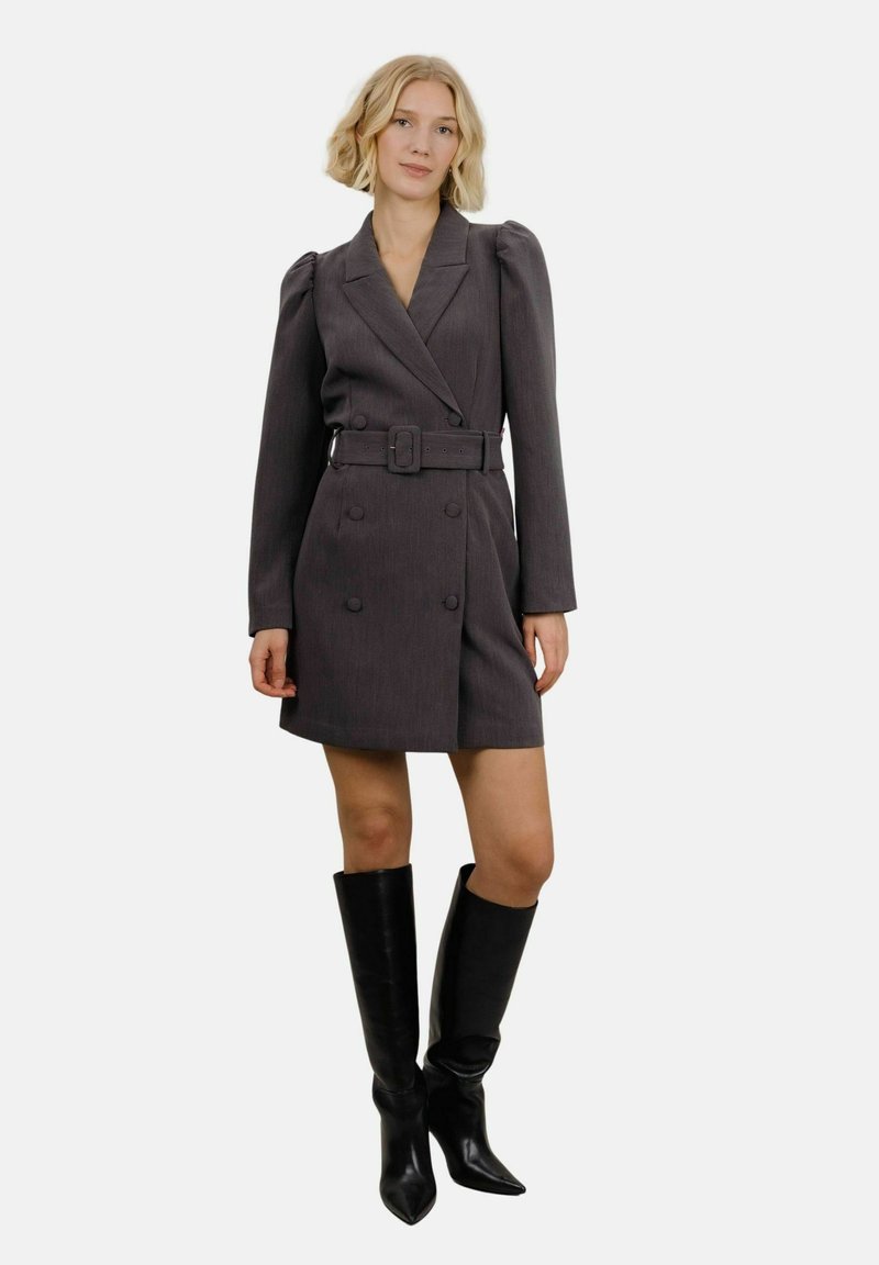 Grå dobbeltbrettet kjole med lange ermer og belte i midjen. Glatt stoff med plisserte skulderdetaljer. Kombinert med høye sorte støvler.