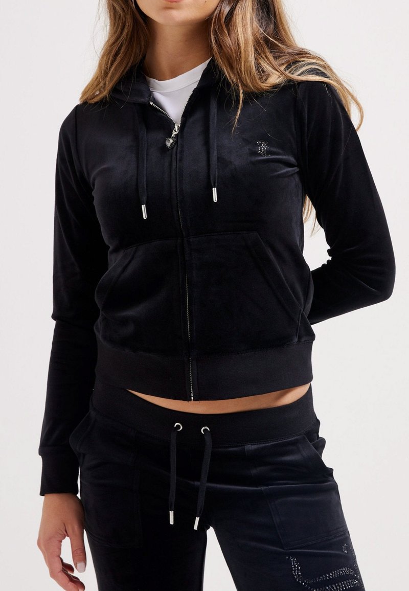 Zwarte rits hoodie van zacht fluwelen materiaal met voorzakken en capuchon met trekkoord, gecombineerd met bijpassende broek met trekkoord. Gladde textuur.