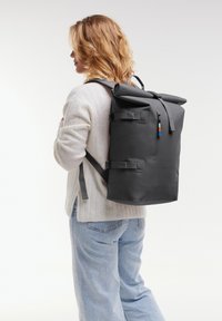 Szary plecak z podnoszonym klapem, z regulowanymi paskami, kieszenią na zamek i kolorowymi akcentami. Wykonany z trwałego materiału o gładkiej teksturze.