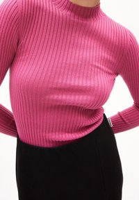 Tight ribbad polotröja i klarrosa, med hög hals och långa ärmar, i kombination med en svart kjol.