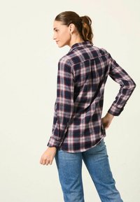 Long-sleeve plaid shirt in navy, red, and cream. Features a collar and buttoned cuffs. Made of woven fabric with a relaxed fit.