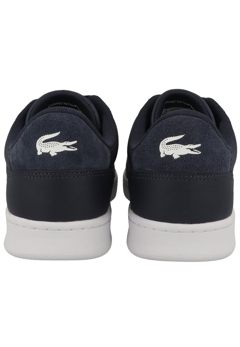 Baskets en suede et cuir bleu marine avec semelles en caoutchouc blanc. Présentent un logo crocodile blanc sur le talon. Design à bout rond, style minimaliste.