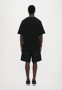 Svart T-skjorte med kort erme og matchende svarte shorts, løs passform, laget av myk stoff, med et enkelt design og ingen synlig merkevare eller mønstre.