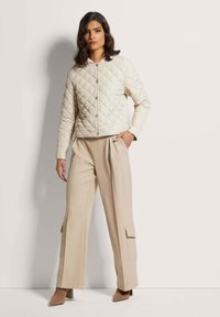 Beige gewatteerde jas met een ronde hals en drukknoopsluiting, gecombineerd met lichtbeige wijde broek met cargozakken.