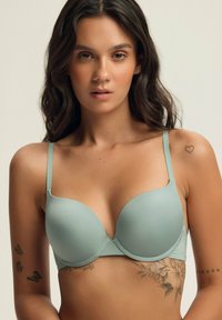 Jasnozielony biustonosz z miękkim wypełnieniem i regulowanymi ramiączkami, gładka tekstura oraz zaokrąglony kształt. Posiada zapięcie na haftkę z tyłu.