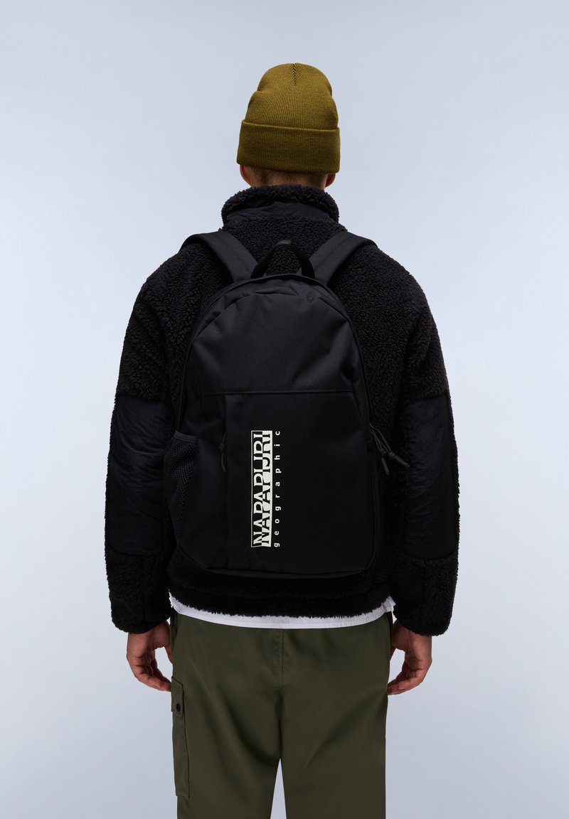 Černý batoh s hladkým povrchem, s výrazným bílým logem, nastavitelnými popruhy a síťovými bočními kapsami, nošený na osobě.