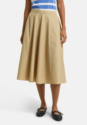 Jupe A-line beige en coton, avec un design plissé et une longueur mi-mollet. Portée avec un haut rayé bleu et blanc et des chaussures noires.