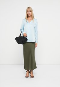 Svetlo modra dolga majica s ovratnikom, v kombinaciji z olivno zeleno maksi krilo. Črna torba z gladko teksturo in angularno obliko, elegantni čevlji s peto.