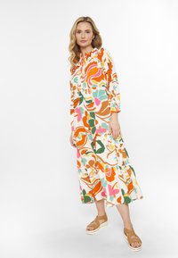 Farbiger Maxikleid mit geschichteter Gestaltung, ausgestattet mit blauen, grünen, rosa und weißen Blumenmustern. Mit einem gerafften Ausschnitt. Beigefarbene Sandalen.