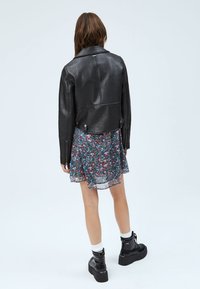 Svart läderjacka med kort modell och slät textur, i kombination med en flerfärgad blommig klänning och svarta plattformskängor.