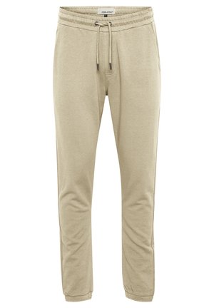 Beige joggerbukser lavet af blødt stof. Har en elastisk talje med snøring og tætsiddende ben. Ingen synlige lommer eller mønstre.