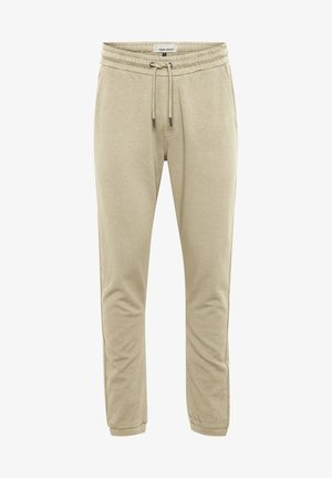 Bež trenirke napravljene od mekanog materijala. Imaju elastičnu struk i vezicu, te su sužene prema nogavicama. Nema vidljivih džepova ili uzoraka.