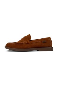Brown suede loafers with a flat sole, featuring a stitched moccasin design and a small branding tag on the side. Simple slip-on style.