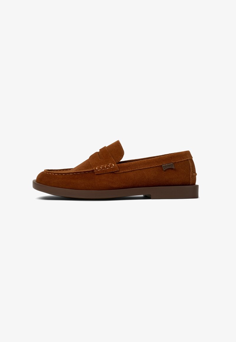 Brown suede loafers with a flat sole, featuring a stitched moccasin design and a small branding tag on the side. Simple slip-on style.