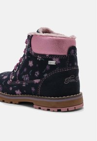 Bottine en daim noir avec accents métalliques roses, motif floral et doublure en fourrure. Elle présente une quincaillerie argentée et une semelle en caoutchouc texturée.