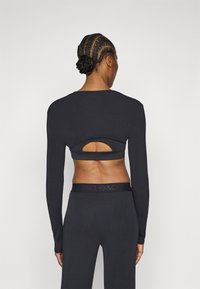 Μακρυμάνικη, σκούρα γκρι μπλούζα με λεπτομέρεια κοψίματος στο πίσω μέρος. Απαλό, ελαστικό ύφασμα· συνδυάζεται με αντίστοιχο σκούρο γκρι παντελόνι με λωρίδα μέσης με λογότυπο.