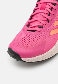 Zapatilla deportiva rosa con parte superior de malla transpirable, diseño texturizado, cordones de tela y una entresuela blanca con manchas. Cuenta con suela de goma.