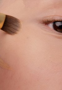 Fundamentapplikation med en blød børste på glat, lys hud. Synlig stribe af flydende foundation langs kæbelinjen.