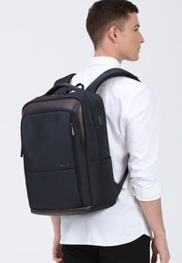 Donkerblauwe rugzak van duurzaam materiaal met bruine accenten, voorzien van meerdere vakken, verstelbare schouderbanden en een stijlvolle, rechthoekige vorm.
