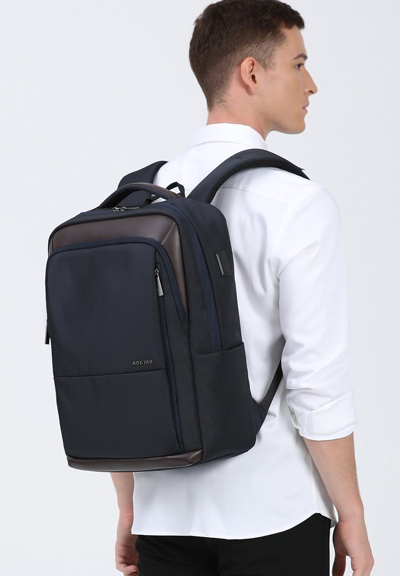 Donkerblauwe rugzak van duurzaam materiaal met bruine accenten, voorzien van meerdere vakken, verstelbare schouderbanden en een stijlvolle, rechthoekige vorm.