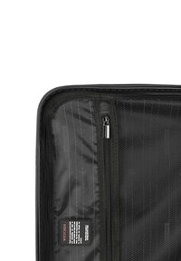 Pochette noire zippée avec un extérieur lisse et mat, dotée d'un motif à rayures diagonales ; inclut une étiquette en tissu avec des informations sur le produit.