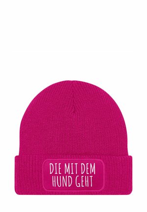 Rosa gestrickte Mütze mit einem umgeschlagenen Bund, der ein rechteckiges Patch mit der Aufschrift "DIE MIT DEM HUND GEHT" in weißer Schrift trägt.