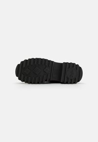 Semelle de chaussure en caoutchouc noir avec un motif de semelle robuste, présentant de profondes rainures et des accents texturés pour une traction et une durabilité améliorées.