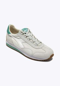 Sneaker grigio chiaro con finitura in suede liscia, accentuazioni verdi sul tallone e sulla linguetta, lacci piatti e suola in gomma testurizzata.