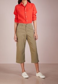 Red linen button-up shirt paired with olive green cropped wide-leg trousers and white sneakers. Simple design with clean lines.