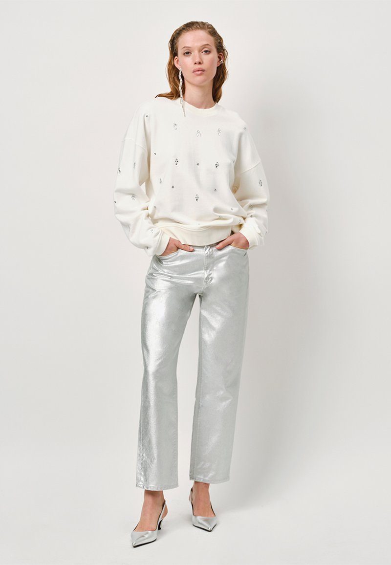 Witte sweatshirt met verspreide versieringen, gecombineerd met glanzende zilveren wijde broeken en zilveren puntige hakken. Gladde texturen, ontspannen pasvorm.