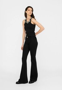 Maiou negru cu decolteu decorat cu mărgele, asortat cu pantaloni evazați negri. Material neted, croială ajustată, design minimalist și accente argintii.