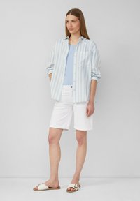 Chemise à rayures à manches longues de couleur bleu clair et blanc, associée à un débardeur bleu clair, un short en denim blanc et des sandales blanches avec une boucle dorée.