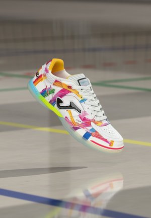 Sneaker bianca con pennellate astratte colorate, logo nero sul lato, fodera interna gialla e suola traslucida su pavimento da campo al coperto.