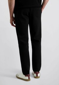 Zwarte sweatpants met een rechte pasvorm, gemaakt van zachte materialen. Heeft een achterzak en wordt gedragen met witte sneakers met bordeauxrode accenten.