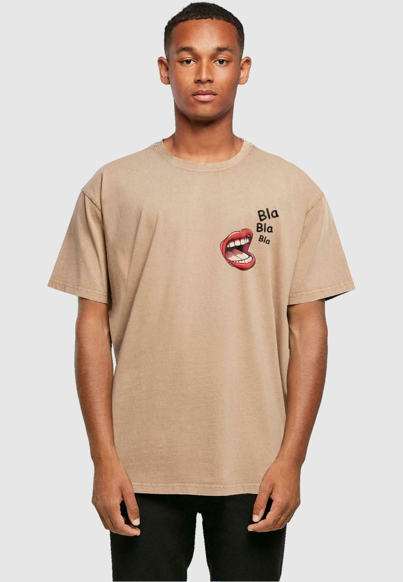 T-shirt beige surdimensionné en coton, avec un graphique d'une bouche rouge et du texte noir "Bla Bla Bla" sur le devant. Manches courtes.