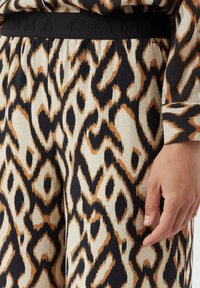 Leopardenmuster-Hosen in Beige, Braun und Schwarz, mit einem schwarzen elastischen Bund mit geprägt Branding und einer strukturierten Stoffoberfläche.